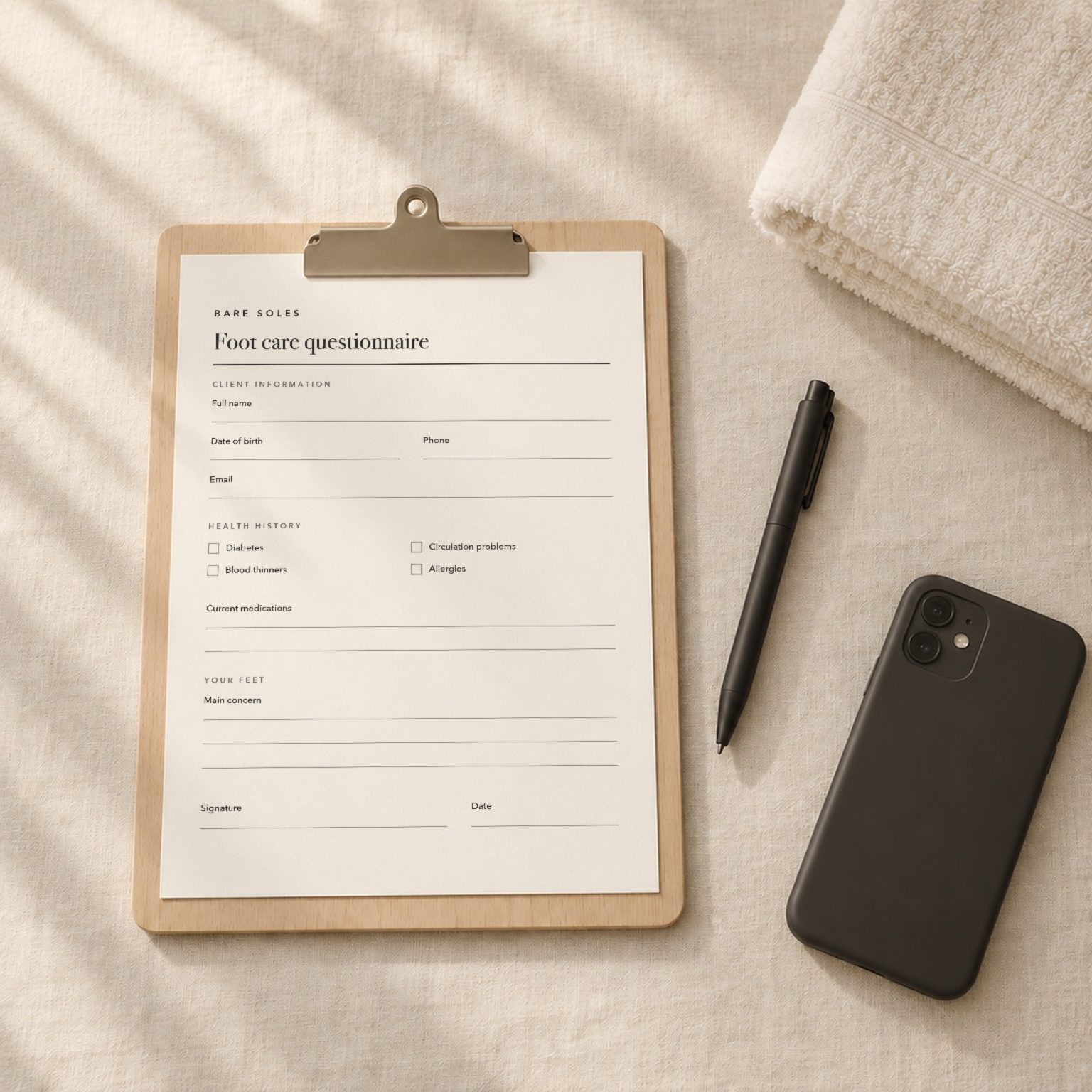 A clipboard holding a Bare Soles foot care questionnaire, with a pen, a phone lying face down and a folded towel on linen
